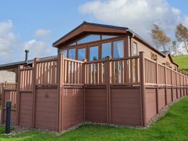 A wooden cabin with a fenced deck on a grassy hill at Dragonfly in Tunstall near Hipswell
