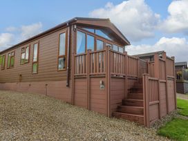 A brown mobile home with large windows and a wooden deck with stairs at Dragonfly in Tunstall near Hipswell