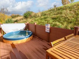 An outdoor deck with a hot tub, a wooden table with chairs, and a chair with a white fabric back at Dragonfly in Tunstall near Hipswell