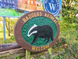 A wooden sign with a badger illustration and the text Badgers Retreat Welcome surrounded by trees and foliage at Dragonfly in Tunstall near Hipswell