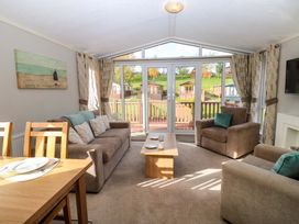 A living room with brown sofas and a wooden coffee table by large glass doors at Dragonfly in Tunstall near Hipswell