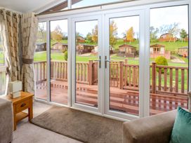 A living room with glass doors opening to a wooden deck and green lawn with cabins in the background at Dragonfly in Tunstall near Hipswell
