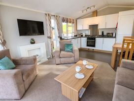 A living room with beige armchairs a wooden coffee table and a kitchen area with white cabinets at Dragonfly in Tunstall near Hipswell