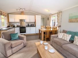 A living room with a sofa and armchair and a dining table and kitchen in the background at Dragonfly Tunstall near Hipswell