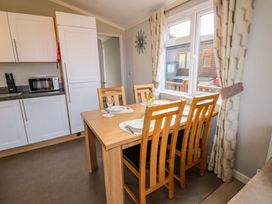 A dining area with a wooden table set for four next to a window and a kitchen with white cabinets in Dragonfly Tunstall near Hipswell