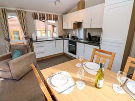 A kitchen and dining area with wooden table set for four and a beige armchair at Dragonfly in Tunstall near Hipswell