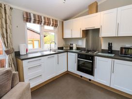 A kitchen with white cabinets a gas stove a toaster a kettle a microwave and a window with striped curtains at Dragonfly in Tunstall near Hipswell