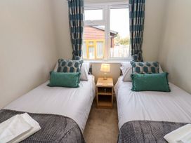 A bedroom with two single beds a nightstand and lamp under a window with curtains at Dragonfly Tunstall near Hipswell
