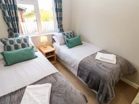 A bedroom with two single beds a wooden nightstand and a window with patterned curtains at Dragonfly in Tunstall near Hipswell
