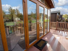 A wooden deck with glass doors leading to the interior and brown railing at Dragonfly in Tunstall near Hipswell