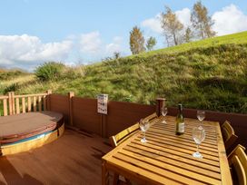 An outdoor wooden deck with a covered hot tub and a table set with wine glasses and a bottle at Dragonfly Tunstall near Hipswell