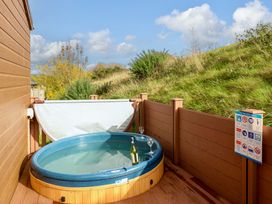 An outdoor hot tub with a bottle and two glasses on a wooden deck with a safety advice sign at Dragonfly in Tunstall near Hipswell