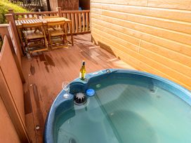 An outdoor deck with a round hot tub filled with water and a wooden table with four chairs at Dragonfly in Tunstall near Hipswell
