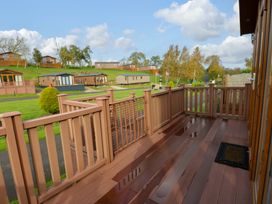 A wooden deck overlooking a village of mobile homes with green grass and trees at Dragonfly in Tunstall near Hipswell