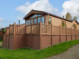 A brown wooden house with a raised deck and railing on grass and gravel at Dragonfly in Tunstall near Hipswell