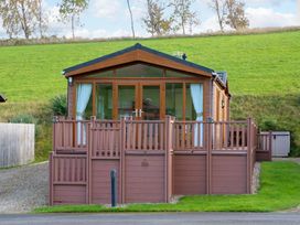 A wooden lodge with glass doors and white curtains on a grassy hill at Dragonfly in Tunstall near Hipswell