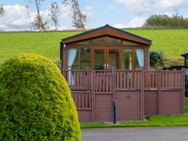 A wooden cabin with large windows and a fenced porch with grass and a shaped bush at Dragonfly in Tunstall near Hipswell