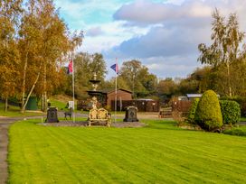 A garden with a fountain bench flags and trimmed bushes near wooden buildings at Dragonfly Tunstall near Hipswell