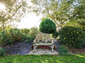 A wooden bench surrounded by trees and bushes in a garden at Dragonfly in Tunstall near Hipswell