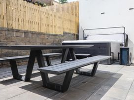 An outdoor area with a table and benches near a hot tub at Golygfa Gele in Llanddulas