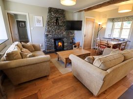 A living room with two beige sofas, a wooden coffee table, a stone fireplace, a wall-mounted TV, and a dining table with chairs at Fox Howe in Thornthwaite