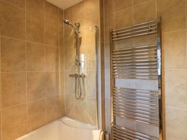 A shower area with a handheld showerhead and a curved glass screen next to a wall-mounted towel radiator in a tiled bathroom at Fox Howe in Thornthwaite