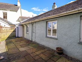 An outdoor patio area with stone paving beside a light grey building with windows and a wooden fence at Fox Howe in Thornthwaite