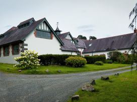 A driveway bordered by grass leading to white buildings with pitched roofs and greenery around at Coach House in Llanwrtyd Wells