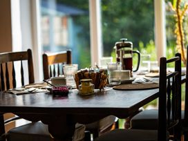 A dining table set with toast, jam, butter, glasses, cups, and a French press in a room with wooden chairs and large windows at Coach House in Llanwrtyd Wells