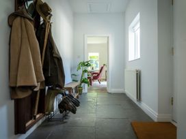 A hallway with coats and boots on a rack a bench a plant a window and a view into a room with a red chair at Coach House in Llanwrtyd Wells