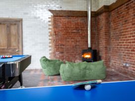 A game room with a blue ping pong table with paddle and ball in the foreground a pool table in the background and green bean bag chairs near a fireplace with a brick wall at Coach House Llanwrtyd Wells