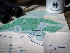 A folded map with marked trails and landmarks next to a pair of black binoculars and a white mug with logo at Coach House in Llanwrtyd Wells