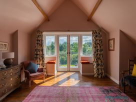 A room with wooden floor a pink rug a leather armchair a wooden chest of drawers a pair of doors with windows and floral curtains at Coach House in Llanwrtyd Wells