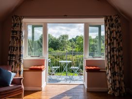 A room with wooden floor and floral curtains overlooking a balcony with a small round table and two chairs at Coach House in Llanwrtyd Wells