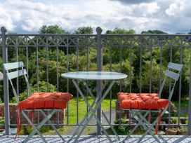 A balcony with a round table and two chairs with orange cushions overlooking a garden at Coach House in Llanwrtyd Wells