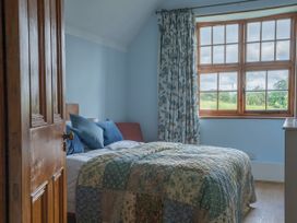 A bedroom with a bed covered in a patterned quilt near a window with floral curtains at Coach House in Llanwrtyd Wells