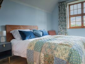 A bedroom with a bed covered with patterned quilt pillows a window with patterned curtains and a bedside table with a lamp at Coach House in Llanwrtyd Wells