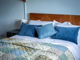 A bed with blue pillows white sheets a patterned quilt a wooden headboard and a bedside table with a lamp at Coach House in Llanwrtyd Wells