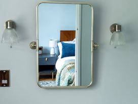 A mirror on a wall reflecting part of a bedroom with a bed blue cushion bedside table and lamp at Coach House in Llanwrtyd Wells
