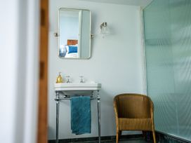 A bathroom with a sink and mirror a wicker chair and a shower area at Coach House in Llanwrtyd Wells