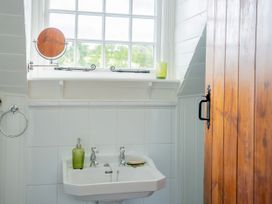 A bathroom sink with separate taps a green soap dispenser and soap near a window and a wooden door at Coach House in Llanwrtyd Wells