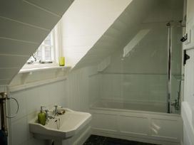A bathroom with a sink, bathtub with shower, and a window on a slanted ceiling wall at Coach House in Llanwrtyd Wells