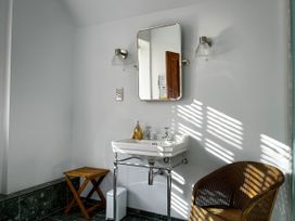 A bathroom with a white sink under a rectangular mirror flanked by two wall lights next to a wooden stool and a wicker chair at Coach House in Llanwrtyd Wells