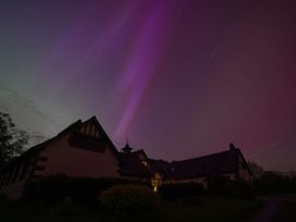 A house at night with purple and green aurora lights in the sky at Coach House in Llanwrtyd Wells