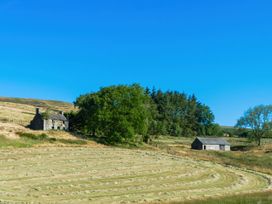 A field with cut grass bordered by trees and two stone buildings at Coach House in Llanwrtyd Wells