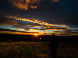 A person standing on grassy land watching the sun set with clouds and hills visible at Coach House in Llanwrtyd Wells