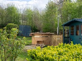 A wooden hot tub next to a green garden shed surrounded by bushes and trees at Coach House in Llanwrtyd Wells