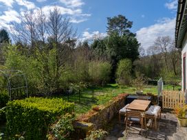 A patio with a wooden table and chairs surrounded by a low stone wall and green trees at Coach House in Llanwrtyd Wells