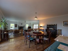 A dining area with a round wooden table and chairs next to a living room with a fireplace and a television at Coach House in Llanwrtyd Wells