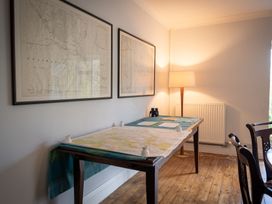 A room with two framed maps on the wall a wooden table with maps and white map weights a floor lamp radiator and wooden chairs at Coach House in Llanwrtyd Wells